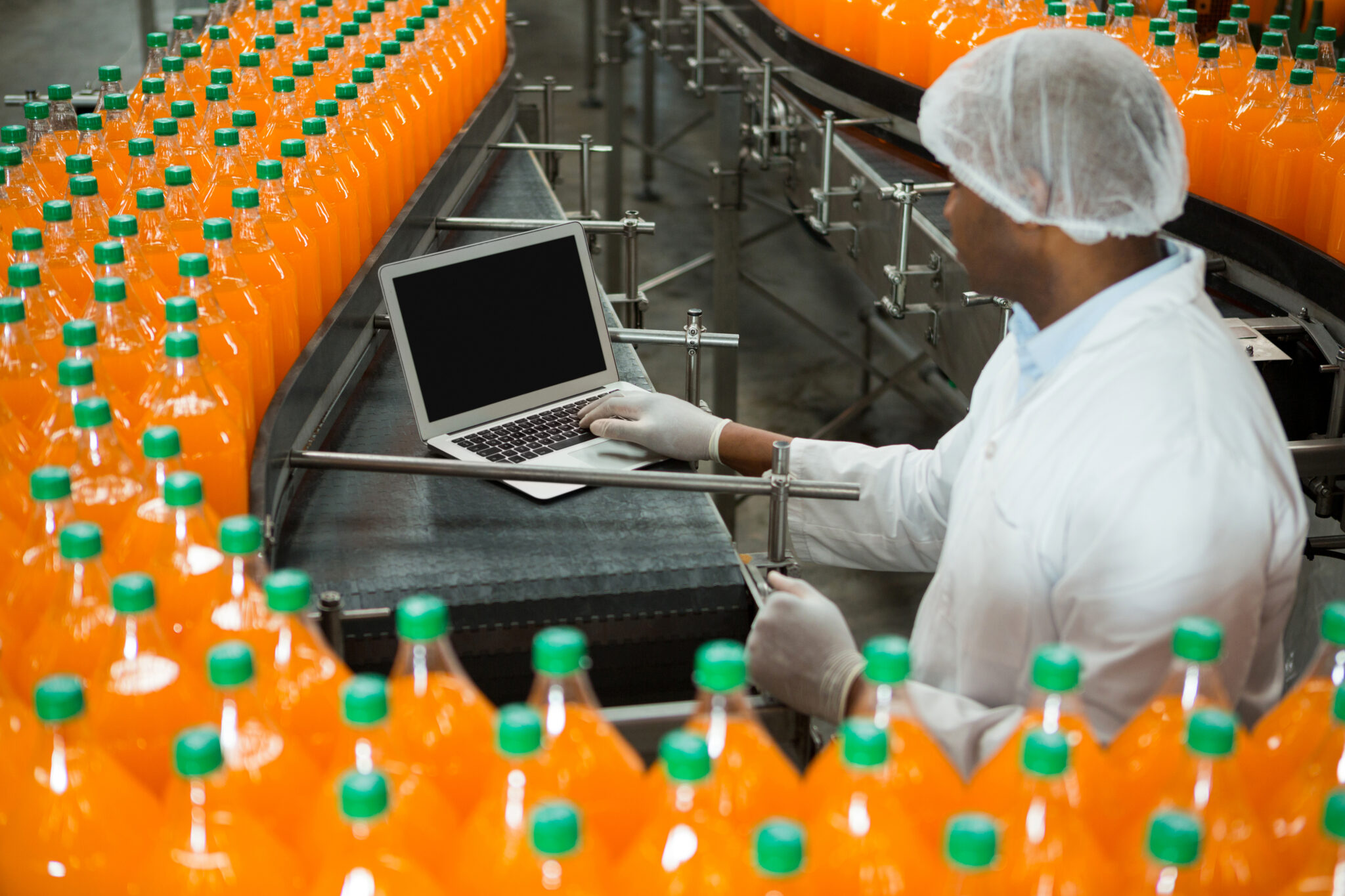 High angle view of male worker using laptop amidst production line in juice factory